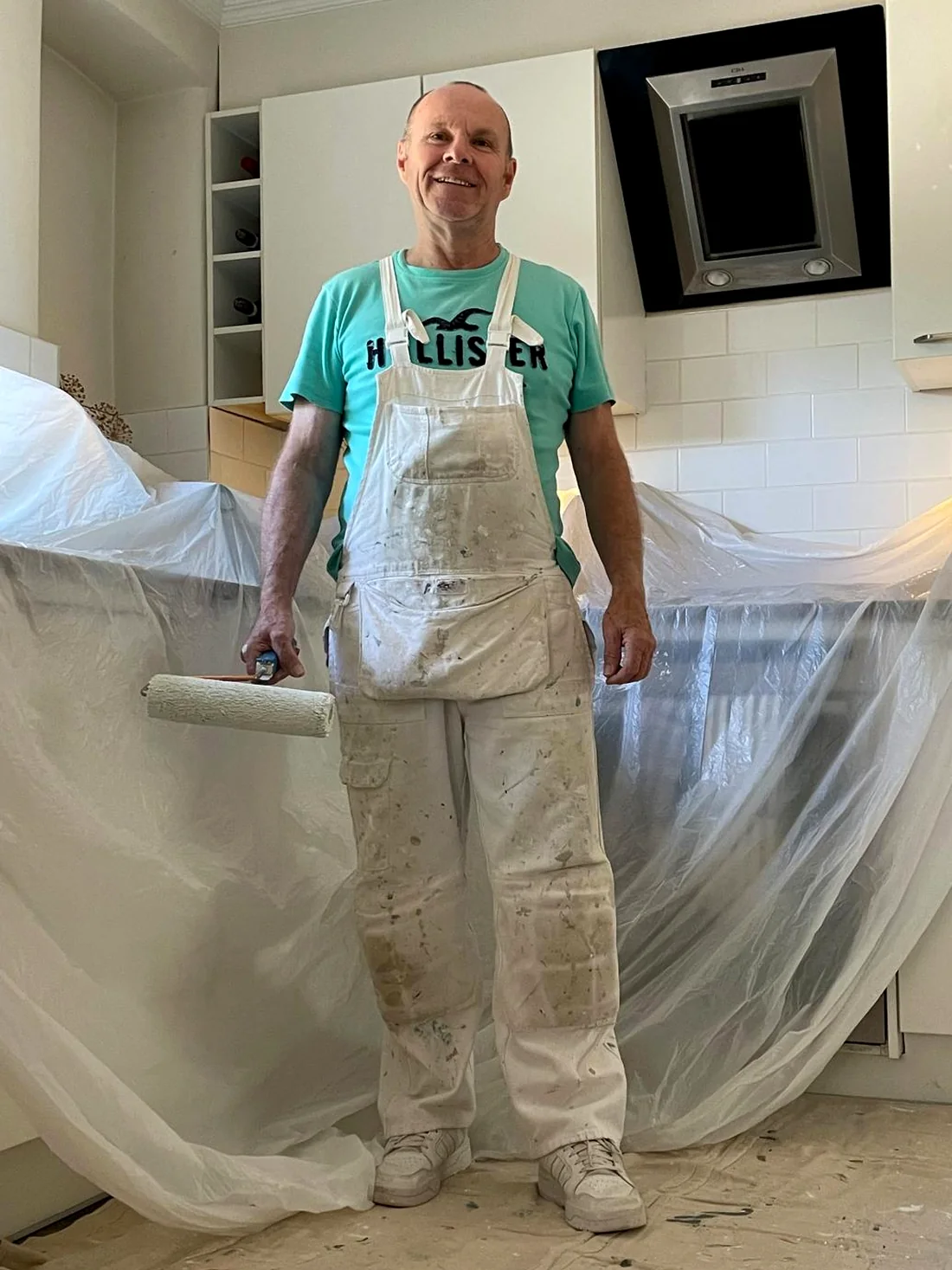 Mark Yeoman in his work whites holding a roller, on a job with the kitchen sheeted up and masked