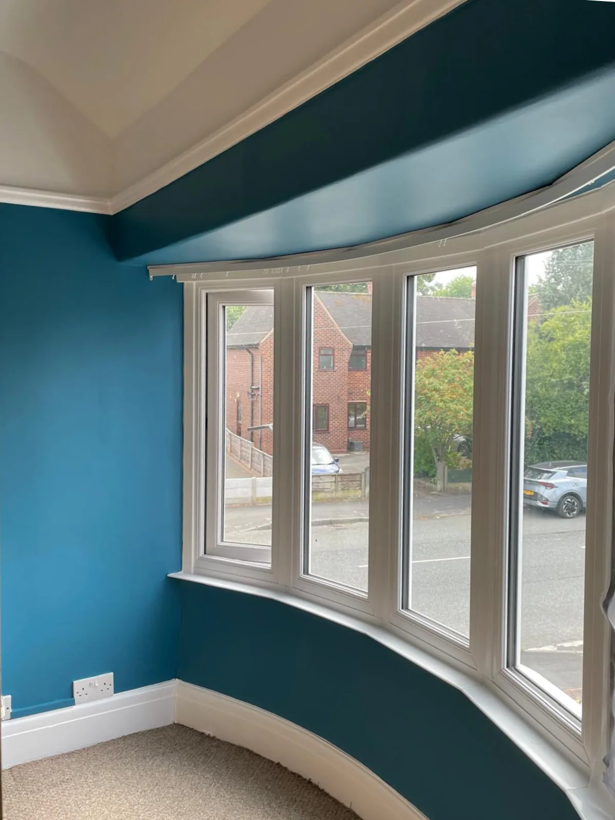 Bay window painted deep teal with crisp white frames and fresh white skirting